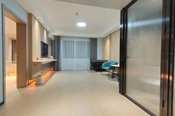 A modern hotel room with a large sliding door, a flat-screen TV mounted on the wall, a small table with a chair, and a large window with curtains. - Alant Hotel (Duyun)