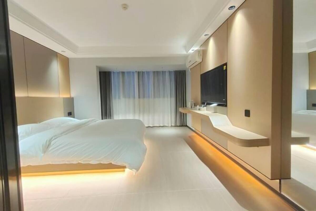 Une chambre d’hôtel moderne dotée d’un grand lit, d’une table de chevet, d’un miroir et d’un téléviseur intégré.