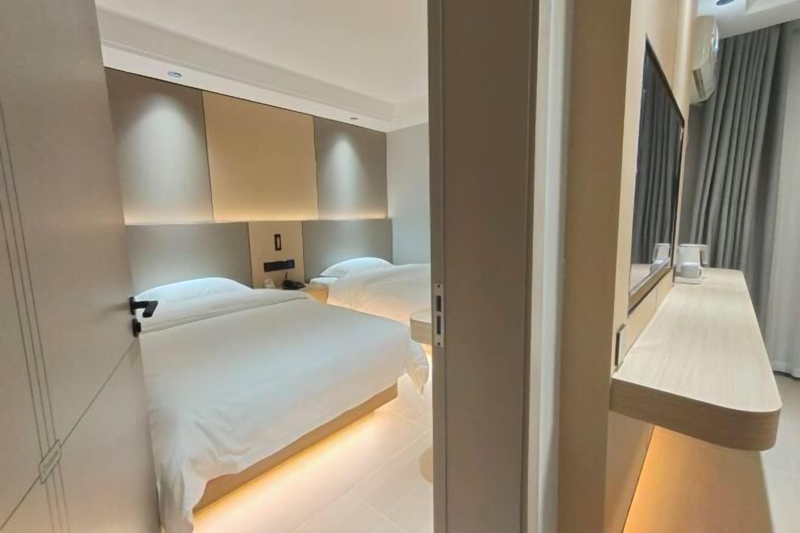 Ein modernes Hotelzimmer mit einem großen Bett, Nachttischen, einem Spiegel und einem fest installierten Schreibtisch mit Stuhl.