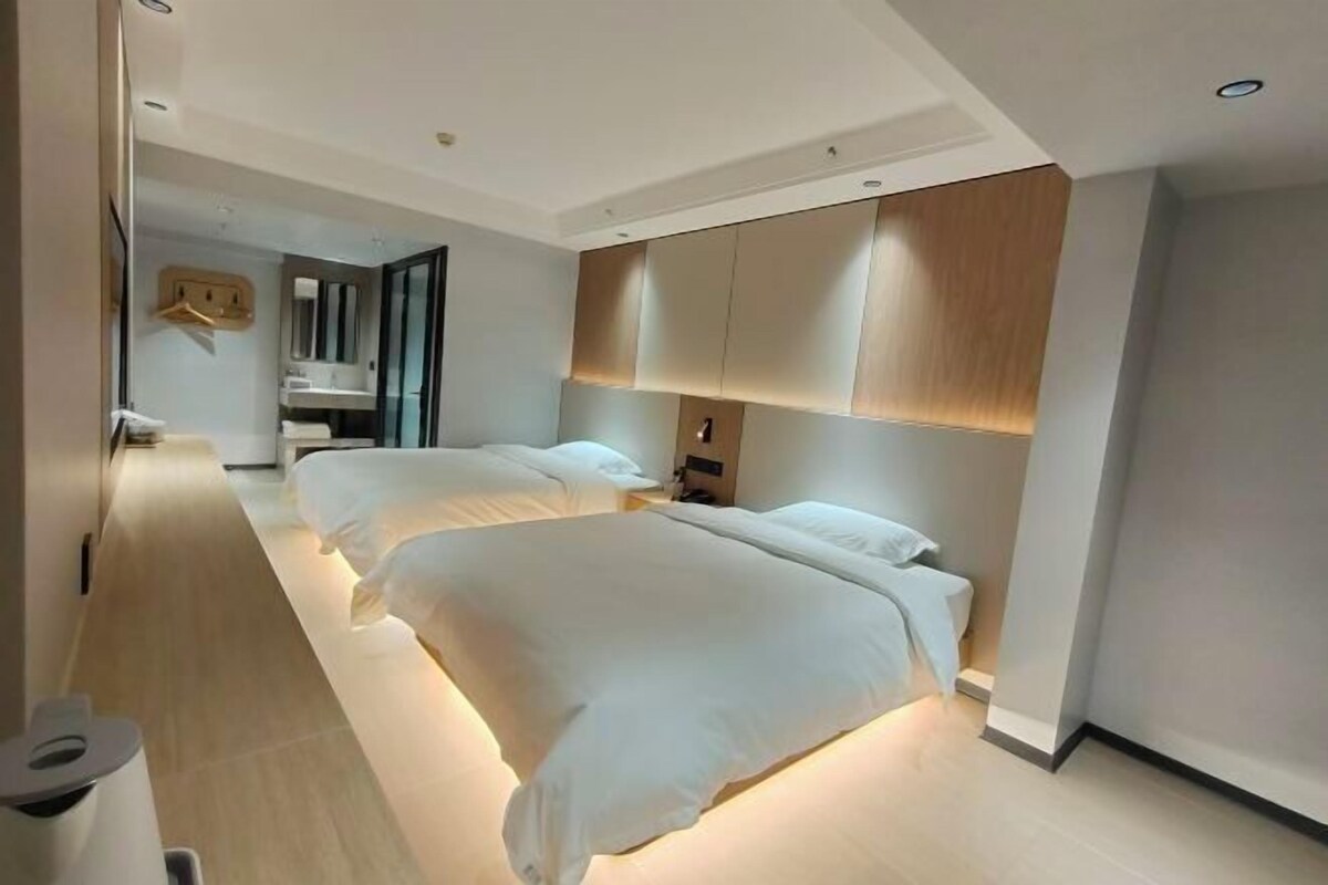 A modern hotel room with two beds, a large mirror, and a wooden headboard.