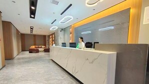 A reception area with a marble reception desk, a sofa, and a counter with a computer and a green object. - Alant Hotel (Duyun)