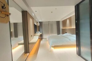 A modern hotel room with a large bed, a bedside table, a mirror, and a sliding door. - Alant Hotel (Duyun)