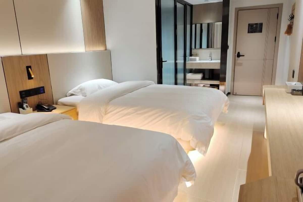 Une chambre d’hôtel avec deux lits, une table de chevet avec un téléphone, un miroir et une armoire.