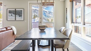 A dining area with a wooden table, benches, and a chandelier. There are framed pictures on the wall and a view of mountains through the windows. - "Tranquil Tamarack" at Tamarack Lodge (Canmore)