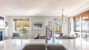 A modern kitchen with a large island, double sinks, and a dining area with a view of mountains. - "Tranquil Tamarack" at Tamarack Lodge (Canmore)
