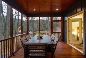 A covered outdoor dining area with a wooden table and benches, surrounded by a wooden deck and railing, overlooking a forested area. - Riverfront Arcade Game Room Pet Friendly Hot Tub (Ellijay)