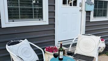 Exterior de una casa con puerta blanca, una corona de bienvenida, buzón y dos sillas de exterior con cojines.