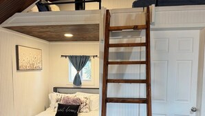 A bedroom with a loft bed, a wooden ladder, a white door, and a window with curtains. - Adorable tiny house (with loft!) near Potosi Live (Abilene)