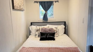 A bedroom with a bed, a window with curtains, a ceiling light, and a wall-mounted picture.