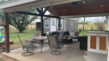 A covered patio with outdoor furniture, a grill, and a small shed in the background.