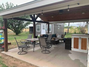 A covered patio with outdoor furniture, a grill, and a small shed in the background.