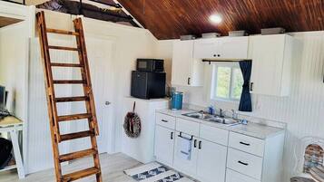 A compact kitchen with white cabinets, a wooden ladder, a microwave, and a sink.