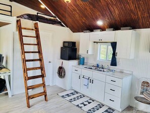 A compact kitchen with white cabinets, a wooden ladder, a microwave, and a sink.