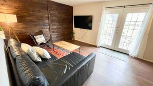 Een woonkamer met een zwarte leren bank, een houten accentmuur, een flatscreen televisie en een schuifdeur van glas.