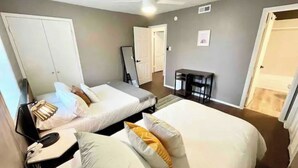 Een hotelkamer met twee bedden, een bureau met stoel, een plafondventilator en een klein tafeltje.