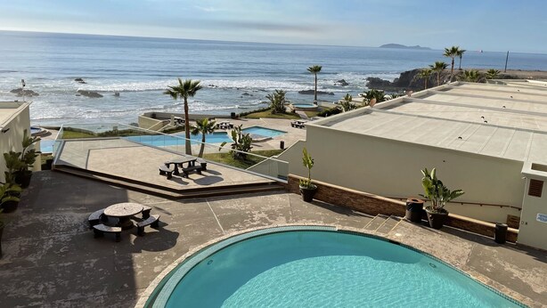 A rooftop pool area with a view of the ocean, palm trees, and a small pool.
