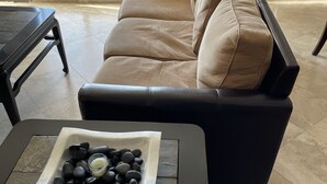 A modern living room with a black leather sofa, a coffee table with a decorative stone centerpiece, and a view of the outdoors through large windows.