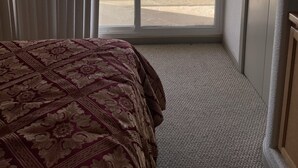 A hotel room with a large bed, a sliding glass door to the beach, and a door to the right.