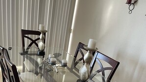 A dining table with a glass top surrounded by dark wooden chairs with cushioned seats.