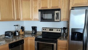 A compact kitchen with wooden cabinets, a microwave, a stove, a dishwasher, and granite countertops.