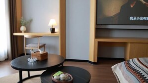 A hotel room with a round black table, a small sofa, a TV on the wall, a lamp, and a plant. - New Times Inn & Hotel (Tongchuan)