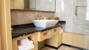 A modern bathroom with a white sink, black countertop, wooden vanity, and a glass shower enclosure. - New Times Inn & Hotel (Tongchuan)