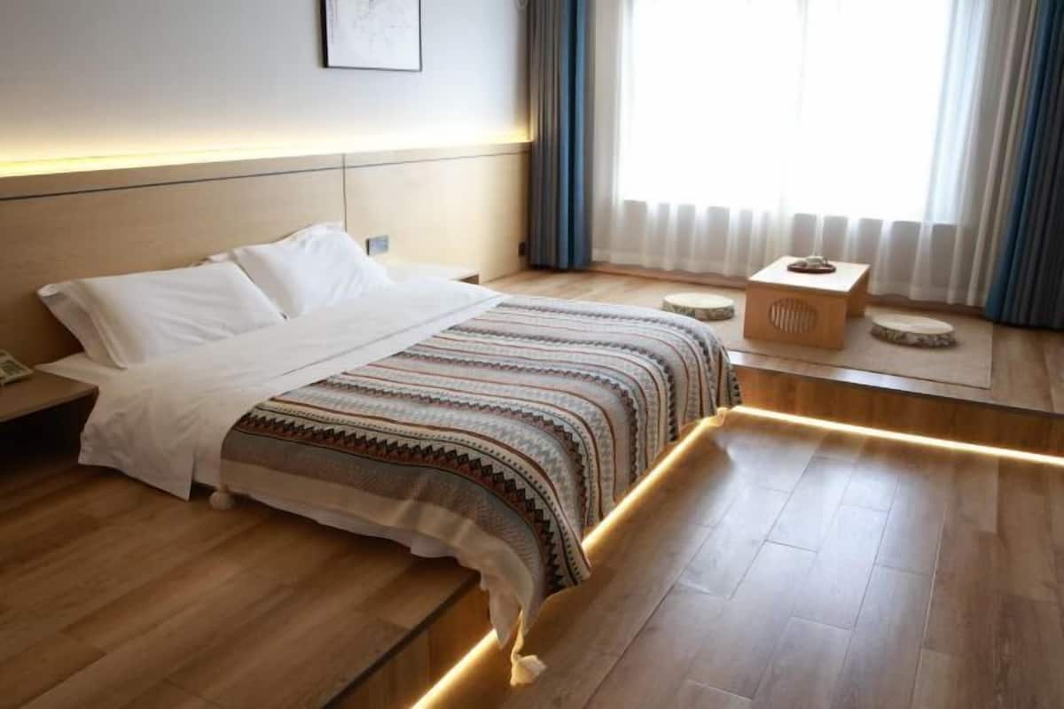 Une chambre d’hôtel moderne avec un plancher en bois, un grand lit recouvert d’une couverture à motifs, une table de chevet et une petite table de nuit en bois.