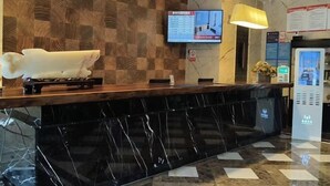 A hotel reception desk with a marble counter, a wooden wall, a television screen, and a digital information kiosk. - New Times Inn & Hotel (Tongchuan)