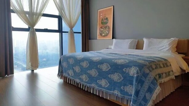 A bedroom with a large bed, sheer curtains, and a city view. - New Times Inn & Hotel (Tongchuan)