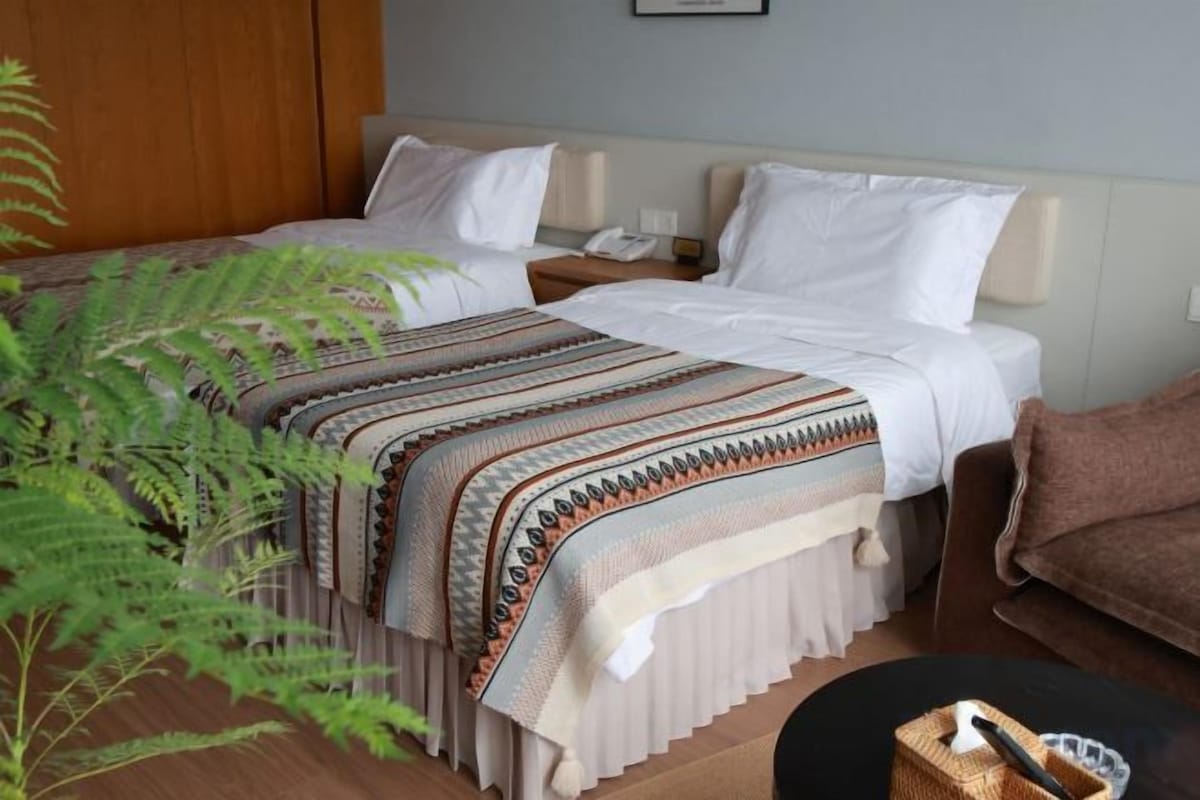Een hotelkamer met een bed, nachtkastjes, een lamp, een plant en een bruine bank.
