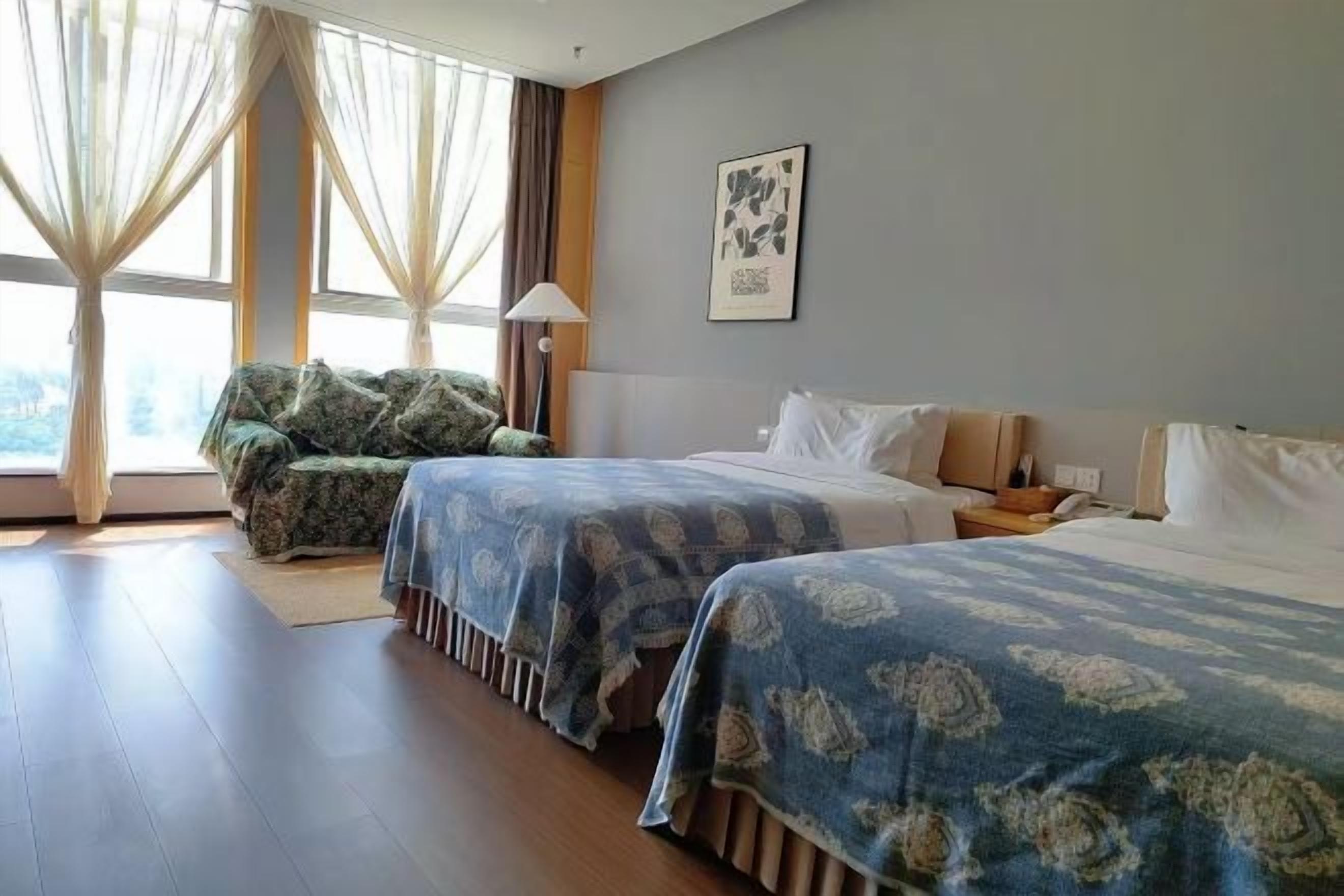 Ein Hotelzimmer mit zwei Betten, einem Sofa und einem großen Fenster mit Vorhängen.