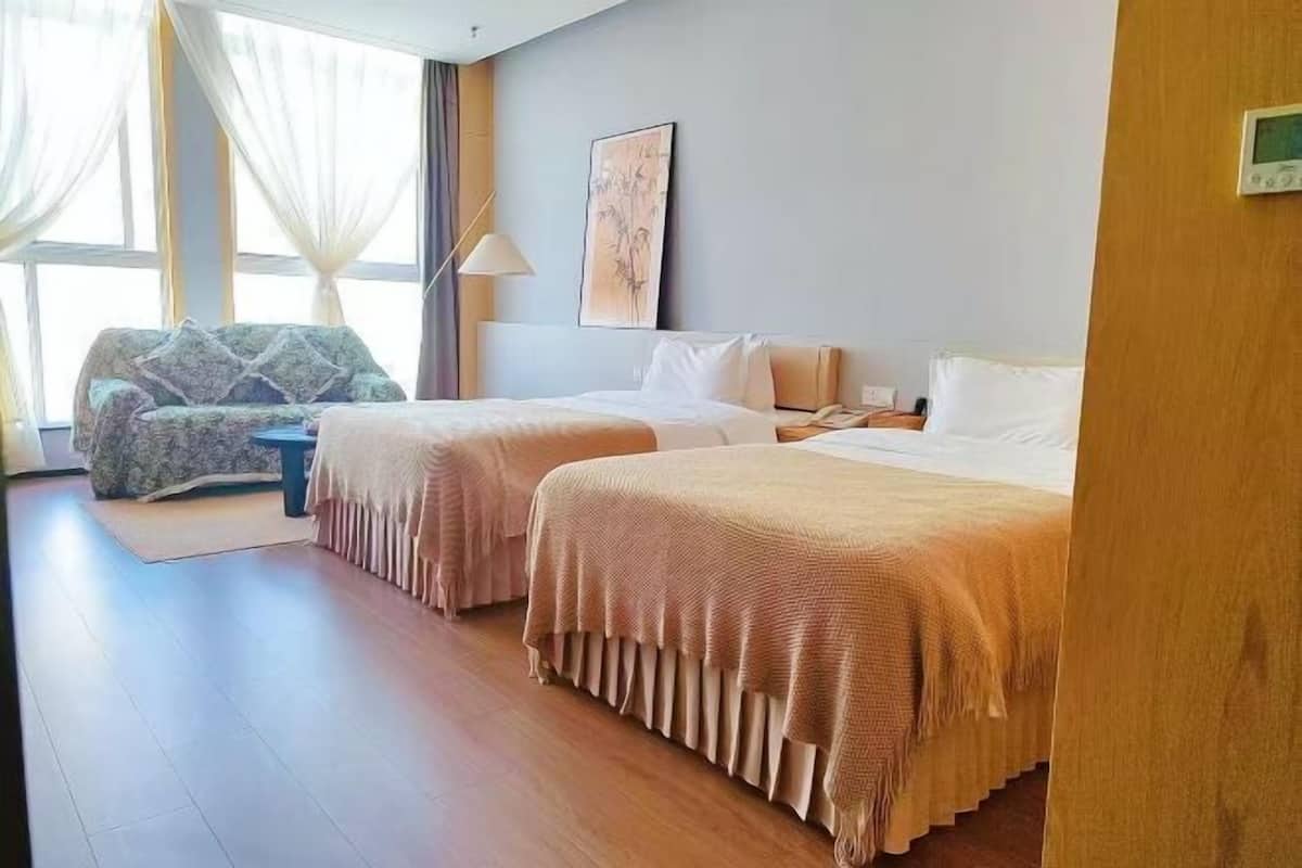 Une chambre d’hôtel avec deux lits, un canapé, une lampe et une fenêtre avec des rideaux.