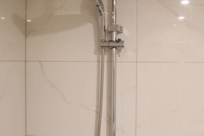 Experience a sleek bathroom with a chrome showerhead and handheld shower attachment, set amidst glossy tiles.