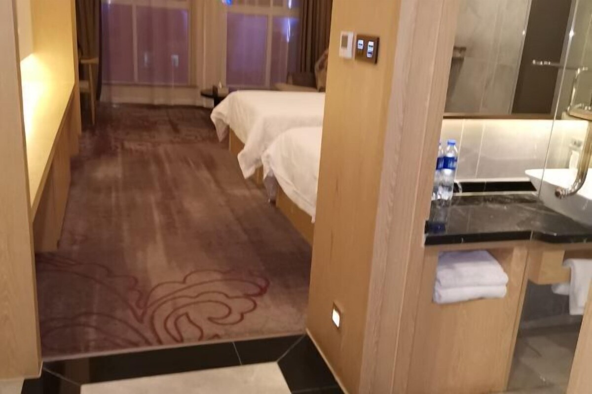 A hotel room with two beds, a bathroom with a mirror and sink, and a wooden floor.
