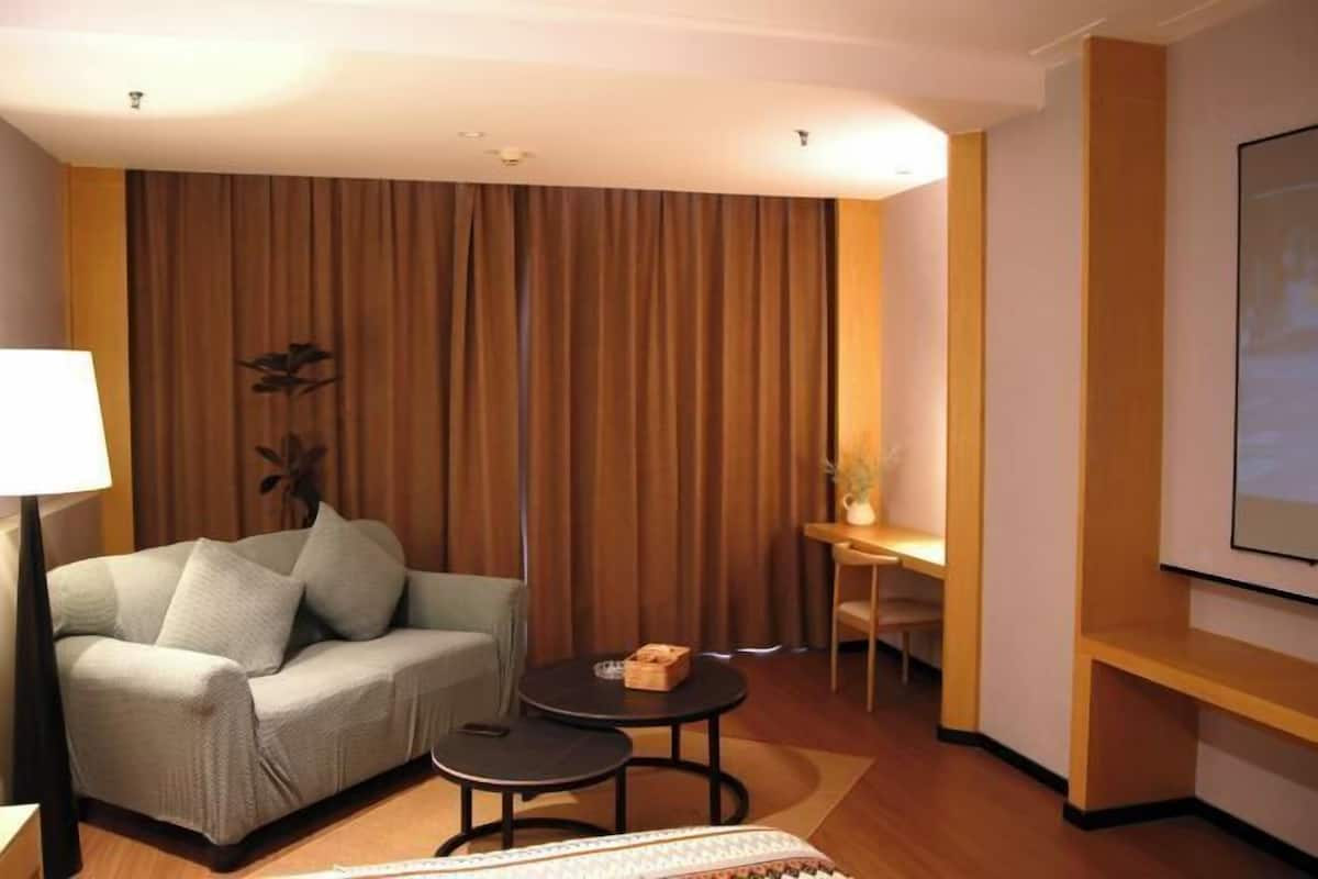 Une chambre d’hôtel avec un canapé, une petite table, une lampe et un téléviseur fixé au mur.
