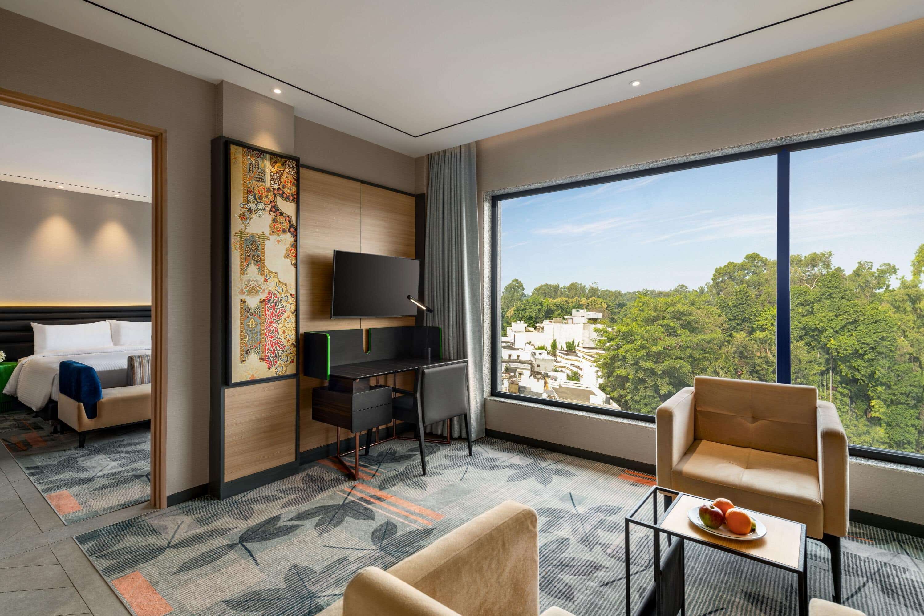 A modern hotel room with a large window, a desk, a bed, and a sofa.