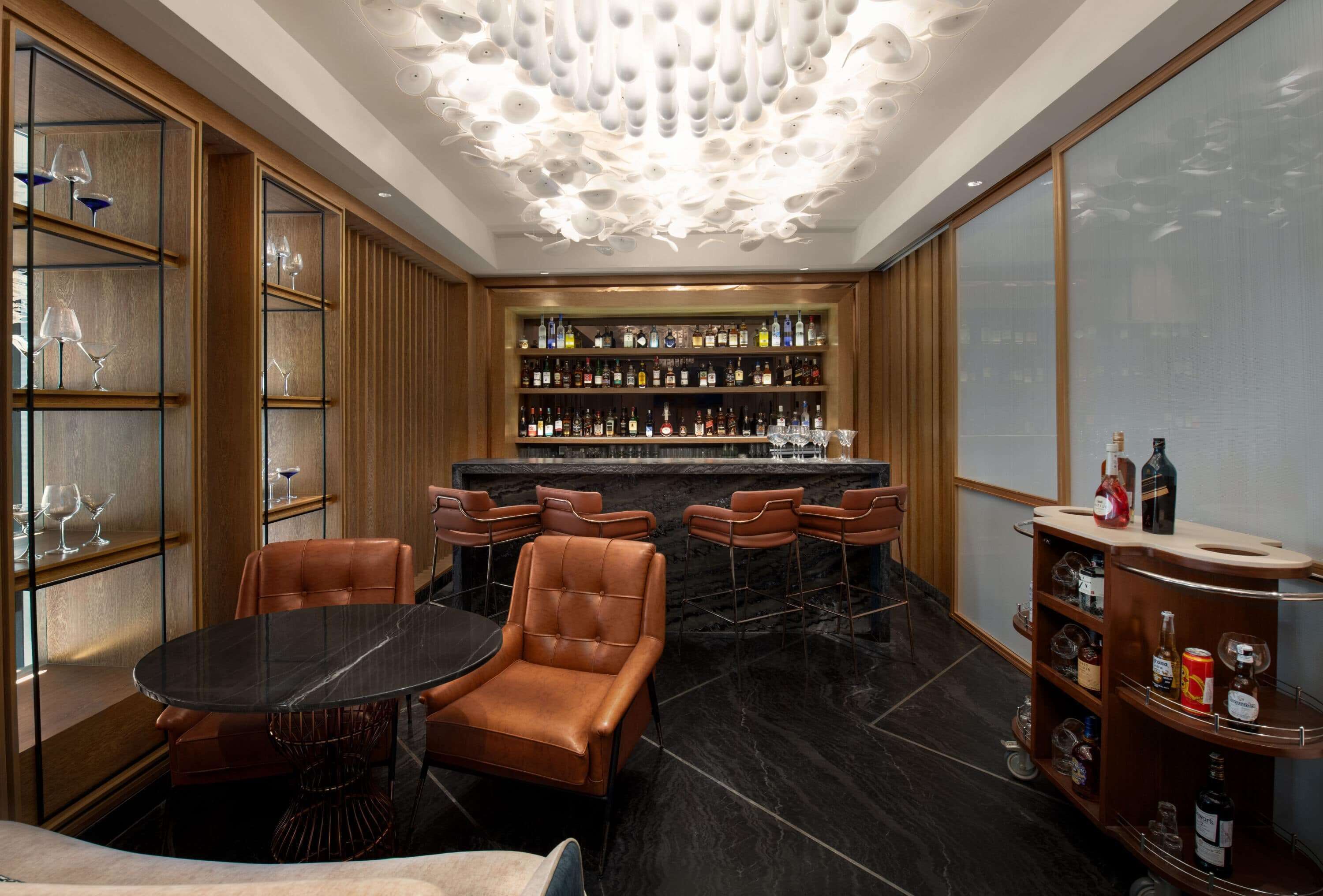 A bar area with leather chairs, a marble table, and shelves stocked with bottles.