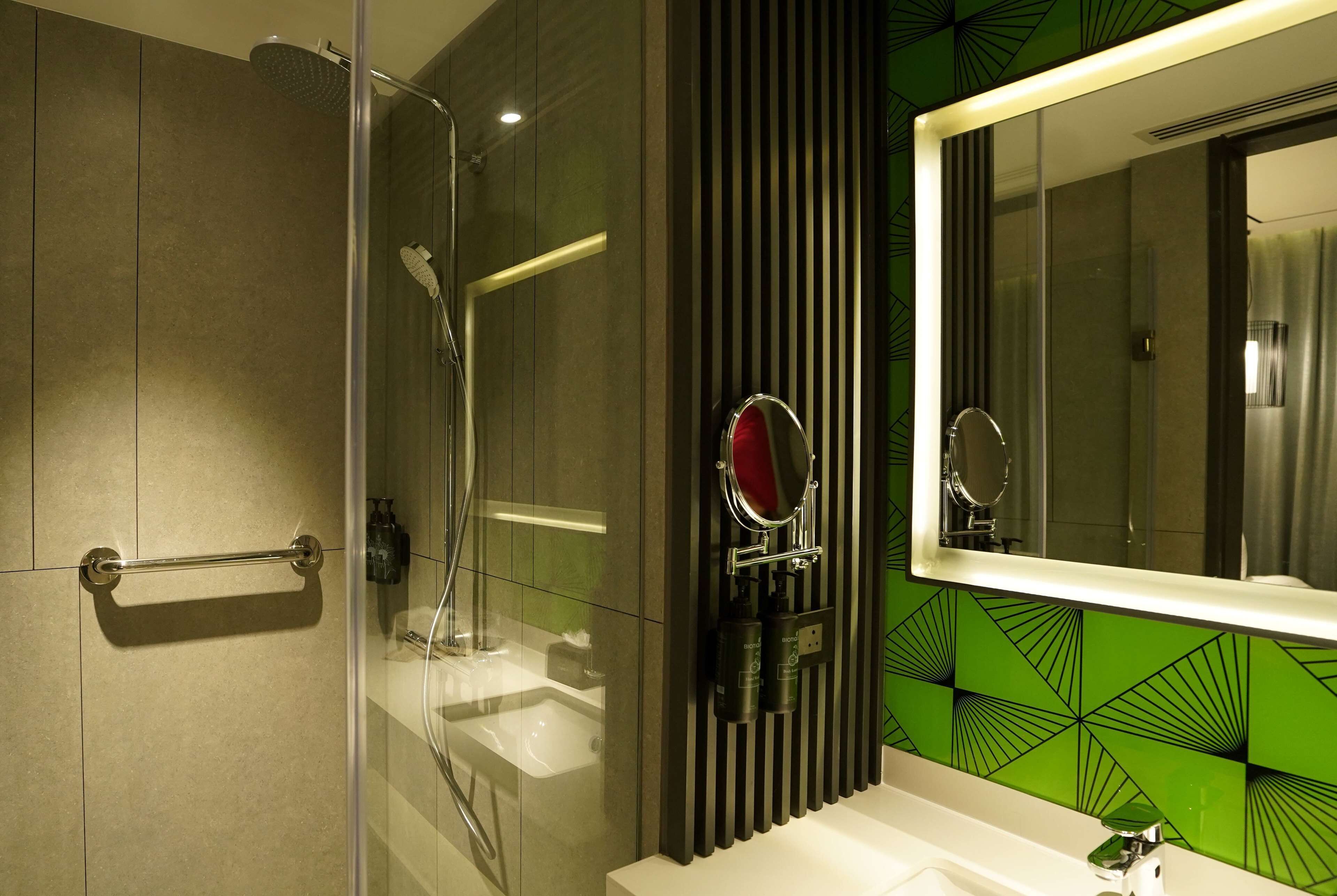 A modern bathroom with a glass shower enclosure, a vanity with a mirror, and a green patterned wall.