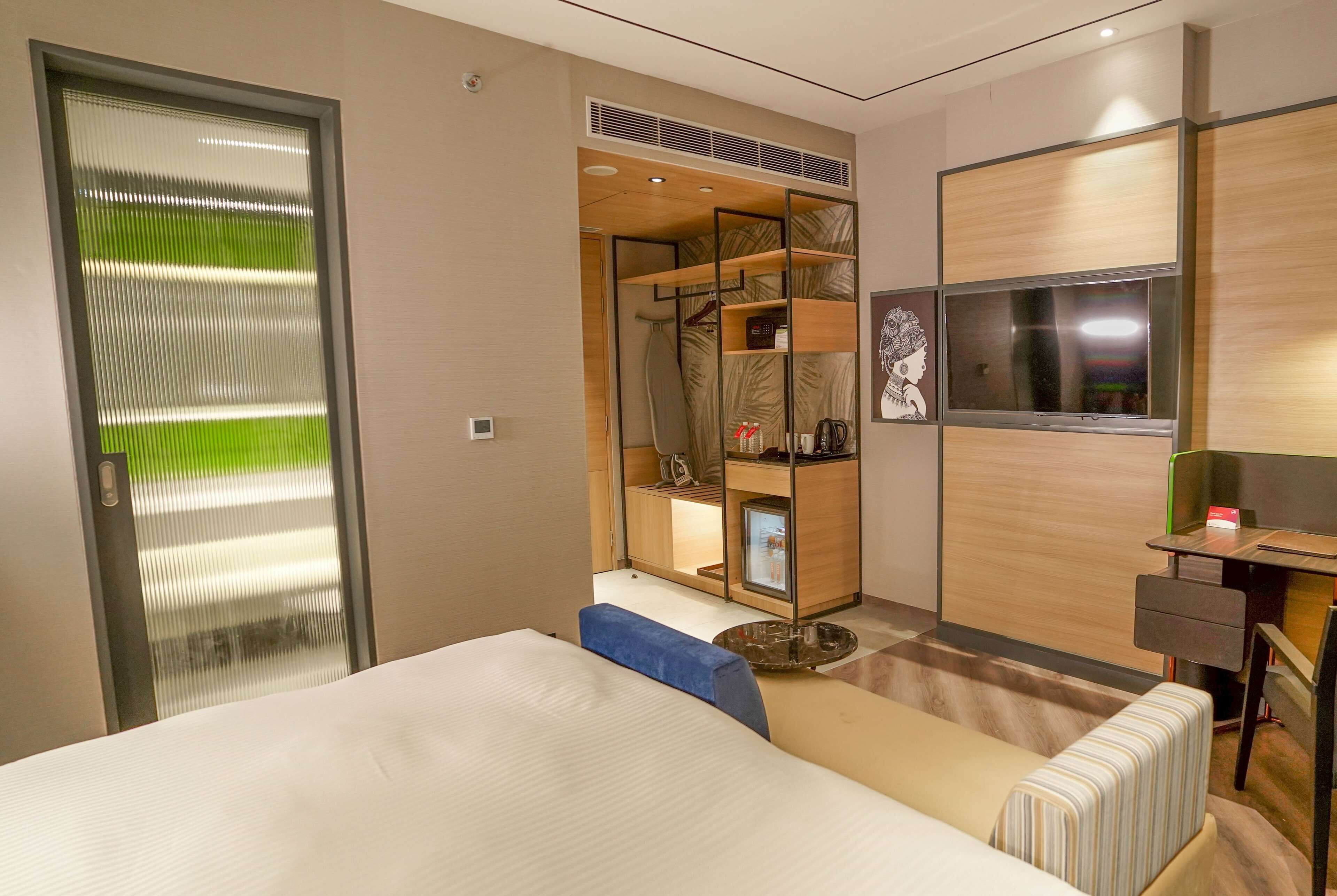 Una habitación de hotel moderna con una cama grande, un área de descanso, un armario con estantes, un escritorio y una televisión.