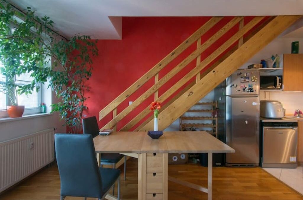 A kitchen with a wooden staircase, a dining table with chairs, a refrigerator, and a sink.