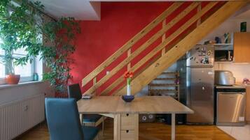 A kitchen with a wooden staircase, a dining table with chairs, a refrigerator, and a sink.