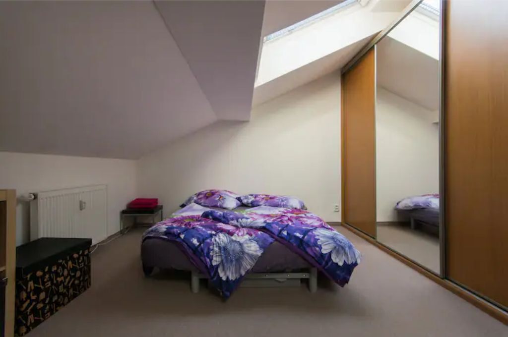 A bedroom with a bed, a small table, a radiator, and a large mirror.