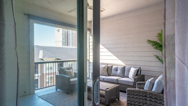 A balcony with wicker furniture, a sliding glass door, and a view of a building in the background.