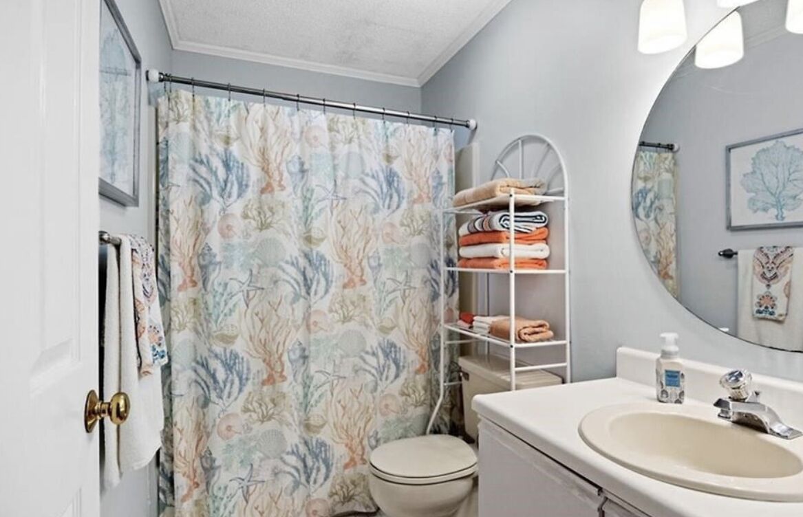 A bathroom with a shower curtain, a toilet, a sink, and a shelf with towels.