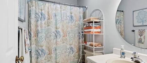 A bathroom with a shower curtain, a toilet, a sink, and a shelf with towels.