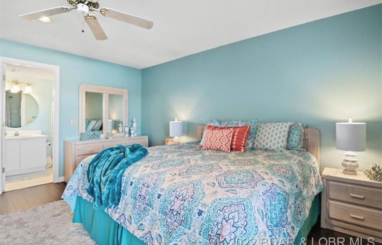 A bedroom with a bed, nightstands, a mirror, and a ceiling fan.