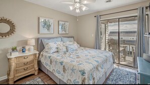 A bedroom with a bed, a ceiling fan, a nightstand, and a view of the outside.