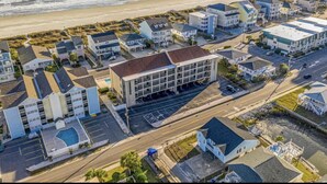 An aerial view of a coastal residential area with multiple buildings, including a large hotel with a swimming pool and parking lot.