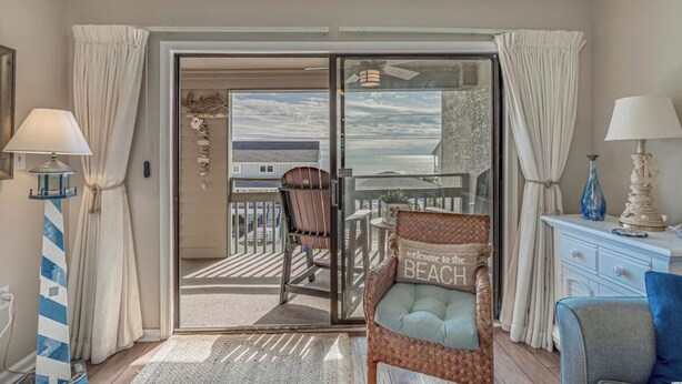 A room with a sliding glass door leading to a balcony, a wicker chair with a cushion, a small table, and a lamp.