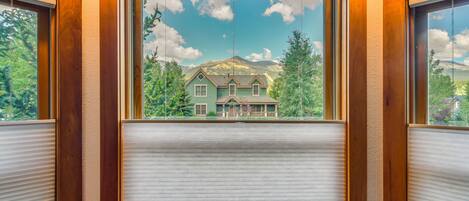 A room with a large window featuring a view of a house and mountains.